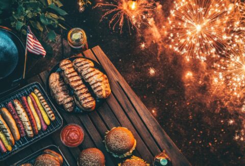 Patriotic Fireworks Feast: A high-angle perspective of a festive, patriotic outdoor meal is lit by a colorful display of fireworks, offering a warm and inviting atmosphere.